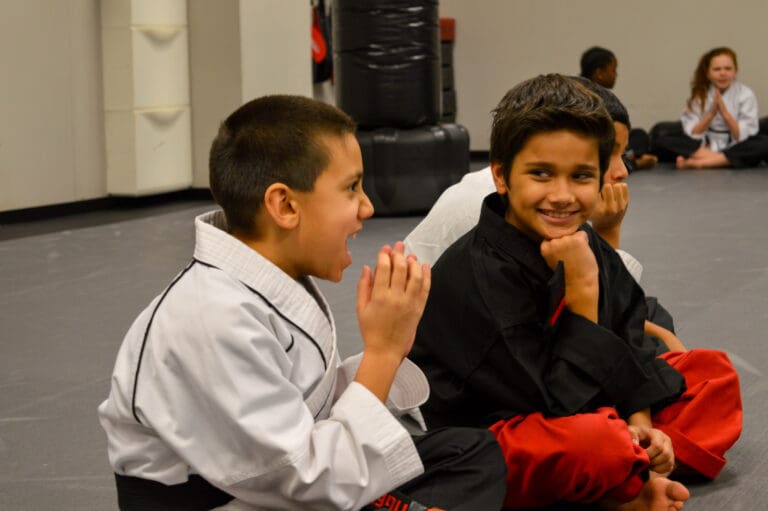 two kids sitting and smiling during karate class at Rise Martial Arts in Pflugerville